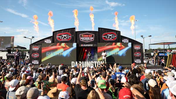 A large crowd gathers in front of a stage with pyrotechnic flame jets at the Cook Out Southern 500 pre-race show at Darlington Raceway, celebrating the track's 75th anniversary.